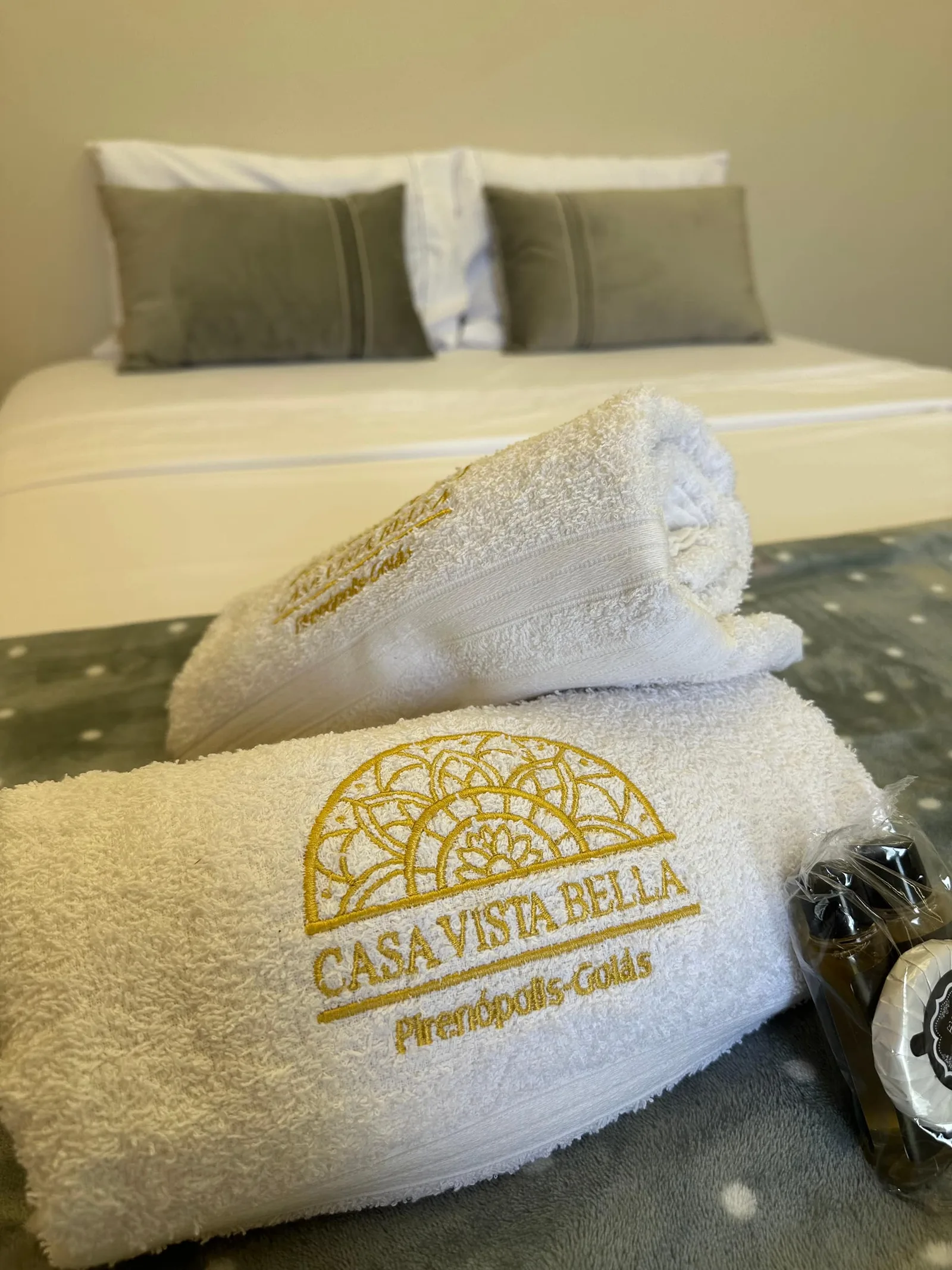 Toalhas Casa Vista Bella dobradas sobre a cama, amenities ao lado